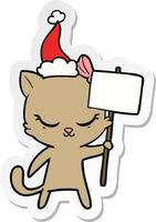 Linda pegatina de dibujos animados de un gato con un cartel con gorro de Papá Noel vector