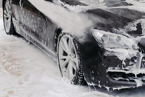 Black auto washed by high pressure of water and soap at carwash. Cleaning service concept. Self service auto wash station photo