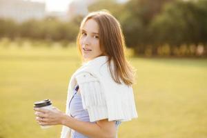 toma lateral de una linda joven con har oscuro, sostiene una taza con café o capuchino, respira aire fresco, disfruta de un ambiente tranquilo, admira la hermosa naturaleza y la puesta de sol. concepto de personas y estilo de vida foto