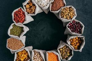 Top view of colorful nutritious cereals and dried fruit in small sacks standing in circle, isolated over dark background. Food concept photo