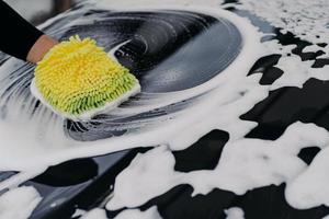 Mans hand washing black car with cloth and soap bubbles. Cleaning automobile. Selective focus. Carwsh concept. photo