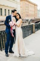 People, happiness and celebration concept. Beautiful young couple in love embrace each other at bridge, have model relationships, celebrate their wedding. Wife and husband have special occasion photo