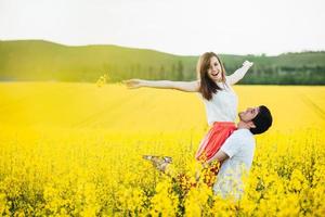 Romantic man raises his girlfriend, enjoy togetherness at beautiful yellow field, pose outdoor, have fun, smile joyfully. Couple in love spend summer holidays at nature. People and harmony concept