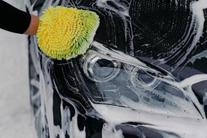 Human hand work concept. Man washes car with soap and cloth. Vehicle cleaning. Close up shot of hand mop washing automobile photo