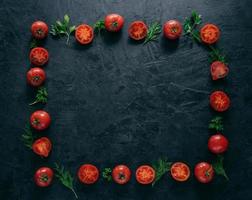 Flat lay of red ripe tomatoes lies in form of frame on dark background with green parsley and dill. Healthy vegeterian dish. Horizontal shot. Copy space for text photo