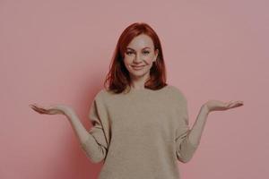 Positive young ginger female comparing two variants options, isolated on pink background photo