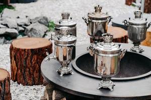 Antique copper samovars on round surface with wooden stumps outdoor. Tea drinking party concept. Russian tradition photo
