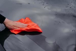 Mans hand cleans surface of black car with microfiber cloth. Maintenance and car wash concept. Professional cleaning. Selective focus photo