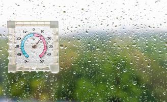 gotas de lluvia y termómetro en vidrio húmedo foto