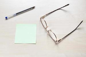 anteojos, pluma en hoja verde en blanco de papel de nota foto
