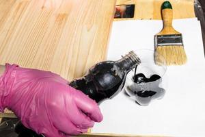 gloved hand pours wood stain from bottle into jar photo