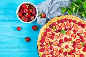 Delicious homemade tart with strawberries and raspberries garnished mint leaves on blue wooden background. Top view photo