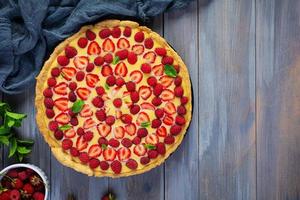 Delicious homemade tart with strawberries and raspberries garnished mint leaves on wooden background. Top view photo