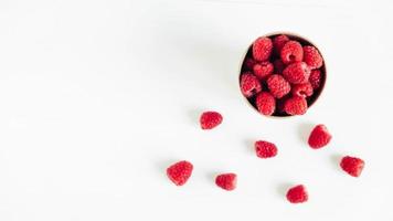 Fresh red raspberries in a paper cup on a white table background photo