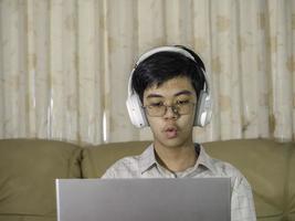 The boy wearing headphones sitting at the table with internet chat skype teacher prepare for exam and using laptop computer for his homework and E-learning for online education. learning kids concept. photo