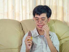 joven asiático con dientes sensibles y helado frío porque come helado en la sala de estar. foto