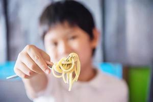 niño come deliciosos espaguetis con salsa de crema - comida italiana con concepto de personas foto