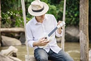 Man play ukulele new to the river- people and music instrument life style in nature concept photo