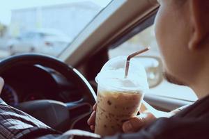 el hombre está bebiendo peligrosamente una taza de café frío mientras conduce un automóvil foto