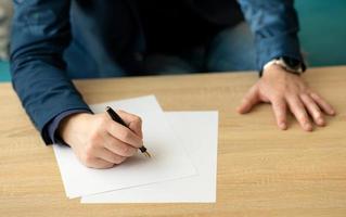 el hombre de negocios en la oficina escribe una carta o firma un documento en un papel blanco con una pluma estilográfica con punta. primer plano de las manos de un hombre de negocios en un traje foto