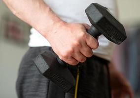 entrenar con pesas en casa. el hombre está entrenando en casa. primer plano de una mano masculina con una mancuerna de 5 kg foto