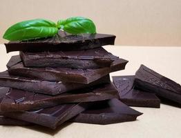 Closeup pieces of dark, inferior chocolate and green basil leaves photo
