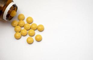 Iron is a very valuable and one of the most important minerals in our body. Front view of a brown bottle with several yellow iron tablets spilling onto on a white background photo