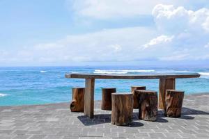 silla y mesa de madera junto al mar con un hermoso paisaje turquesa bajo el cielo azul. foto