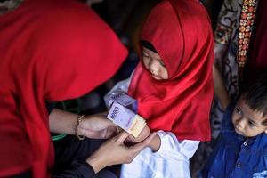 Indonesian people tradition during Eid Mubarak celebration of distributing money or called THR. Asian muslim woman give money to cute boy of family during Idul Fitri. photo
