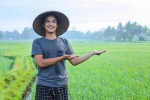 Close-up of Attractive cheerful young Asian farmer standing, smiling and presenting success to growing paddy rice in the rice field. Modern agriculture concept. photo