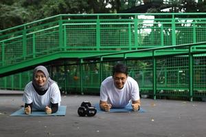Front view of Asian young couple doing plank together on yoga mat at the park. Healthy lifestyle concept. photo