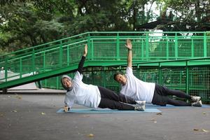 Young Asian muslim couple doing side plank together at the park. Man and woman working out together posing in yoga mat. photo