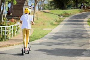 Back view of boy wear helmet enjoy having fun riding electric scooter at street park outdoors on sunny day. Healthy sport children activities outside. photo