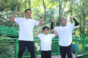 madre y padre jóvenes asiáticos haciendo un gesto de brazo fuerte junto con su hijo en el parque verde. concepto de familia de estilo de vida saludable. foto