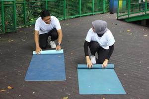 Young Asian couple talking while rolling yoga pilates mat after workout at the park. Healthy lifestyle couple concept. photo