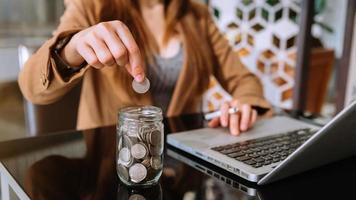 mujer de negocios sosteniendo monedas poniendo en vidrio con el uso de un teléfono inteligente y una calculadora para calcular el concepto de ahorro de dinero para las finanzas foto