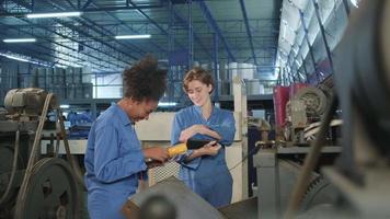 två professionella kvinnliga afroamerikanska och vita elektriska ingenjörsarbetare pratar och skrattar glada medan de inspekterar och underhåller maskiner på tillverkningsfabriken, mekaniska serviceyrken. video