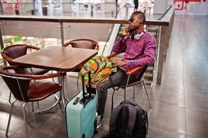 African american man in checkered shirt, sunglasses and jeans with suitcase and backpack. Black man traveler on duty free. photo