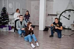 The team of two photographers shooting on studio behind another three workers. Professional photographer on work. One of them joking and holds horns over head. photo