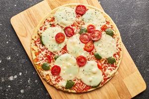 Fast food baked frozen pizza with cheese, tomatoes and pesto. Ready to eat. photo