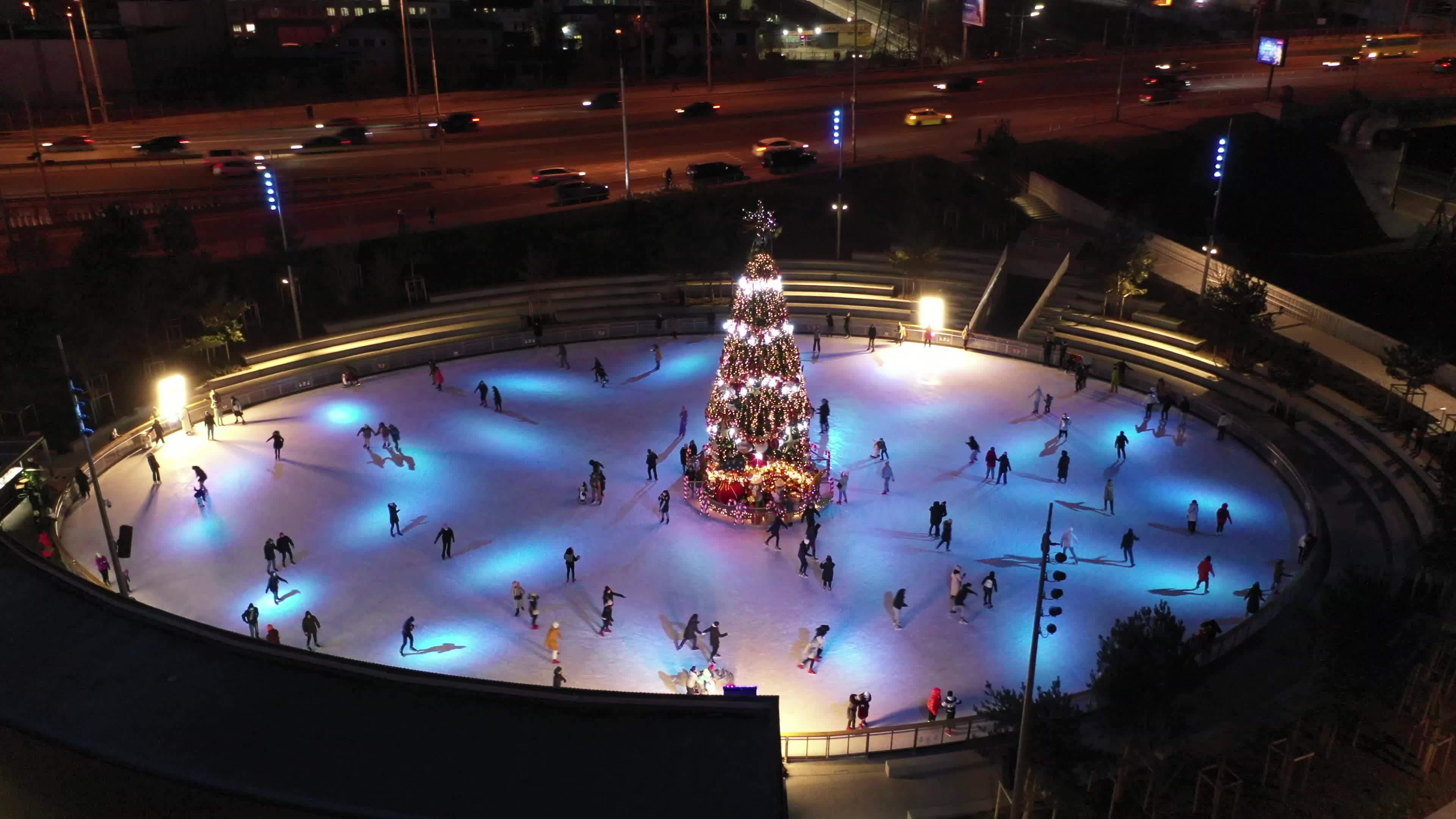 People ice skate around a Christmas tree in a skating rink at night