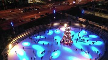 la gente patina sobre hielo alrededor de un árbol de navidad en una pista de patinaje por la noche con un espectáculo de luces video