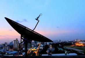 black antenna communication satellite dish over sunset sky in cityscape photo