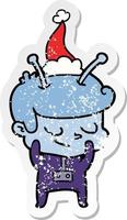 shy distressed sticker cartoon of a spaceman wearing santa hat vector