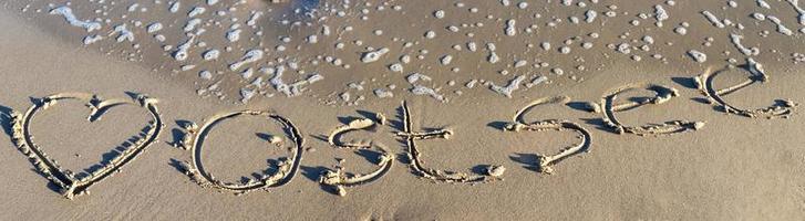 la palabra alemana ostsee mar báltico y un corazón escrito en la arena de la playa. foto