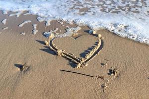 A beautiful heart shape painted into the sand of a baltic sea beach with some water waves. photo