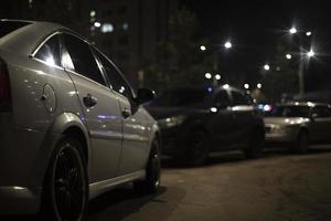 White car in parking lot at night. Lots of cars in yard. Parking space and lights. photo