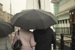 familia con sombrillas negras. la gente llueve los padres con su hija caminan por la ciudad. foto