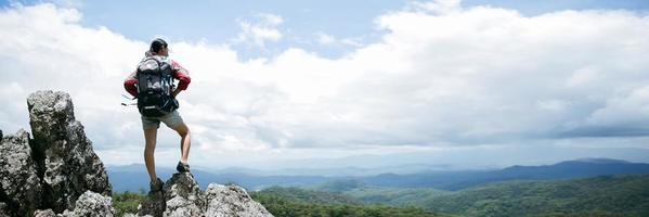 Young person hiking female standing on top rock, Backpack woman looking at beautiful mountain in summer, Landscape with sport girl, panorama hills, forest. Travel and tourism. banner with copy space photo