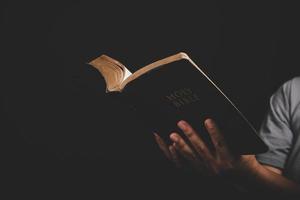 Close up of christian woman hand holding holy bible pray and worship for thank god in church with black background, adult female person are reading book, photo